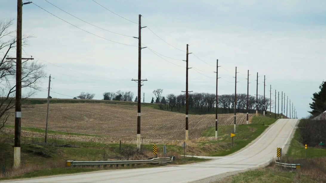 A two-lane highway telephone poles along one side, all with a white-painted section of the pole. 