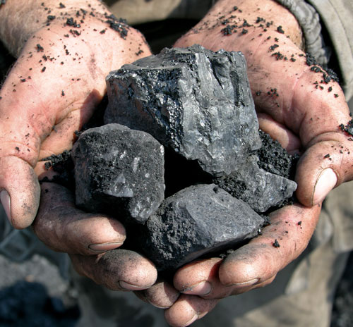A coal miner holds chunks of black coal in his hands.