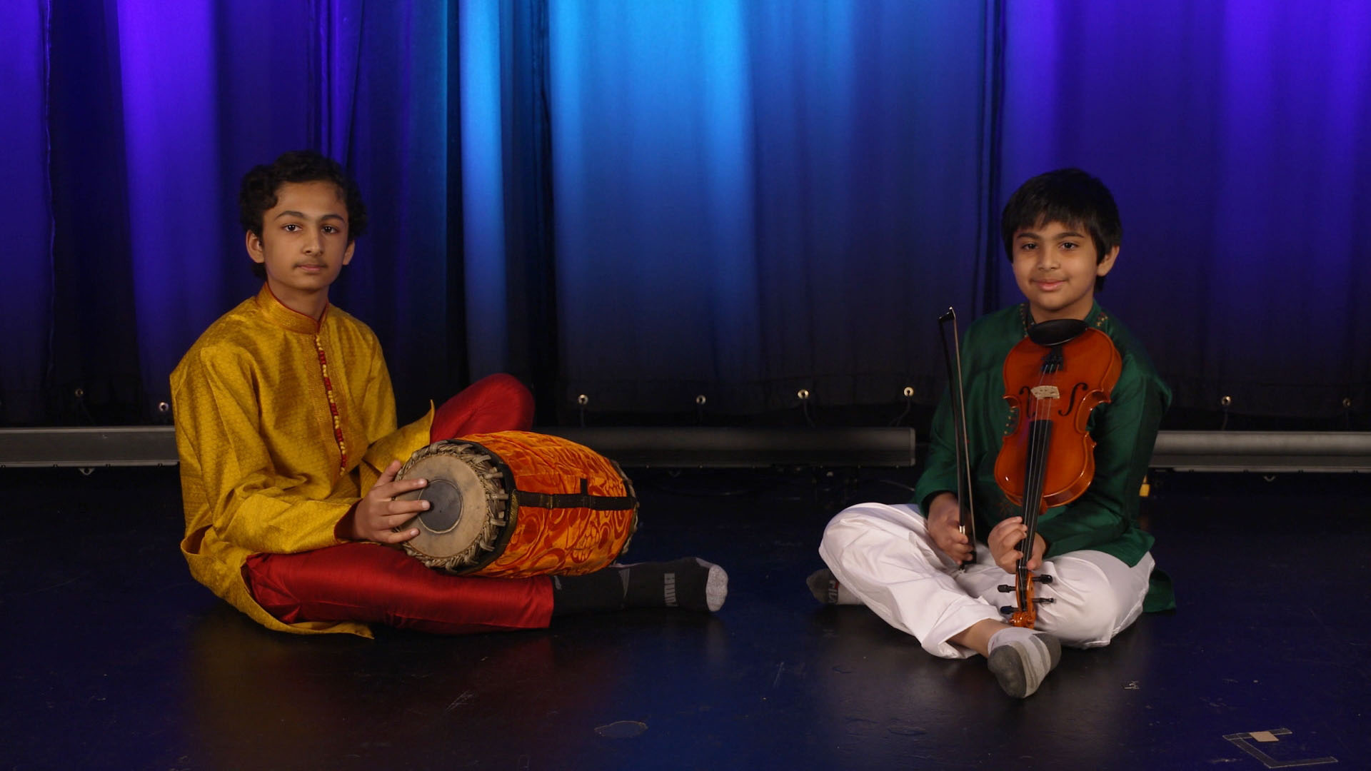 Gonchigar brothers sitting on the ground, one with a traditional drum and one with a violin.