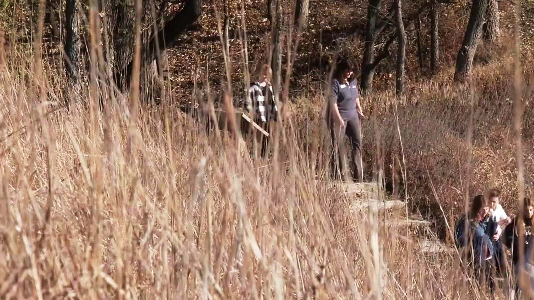 People walking in a trail through a prairie with brown grasses.