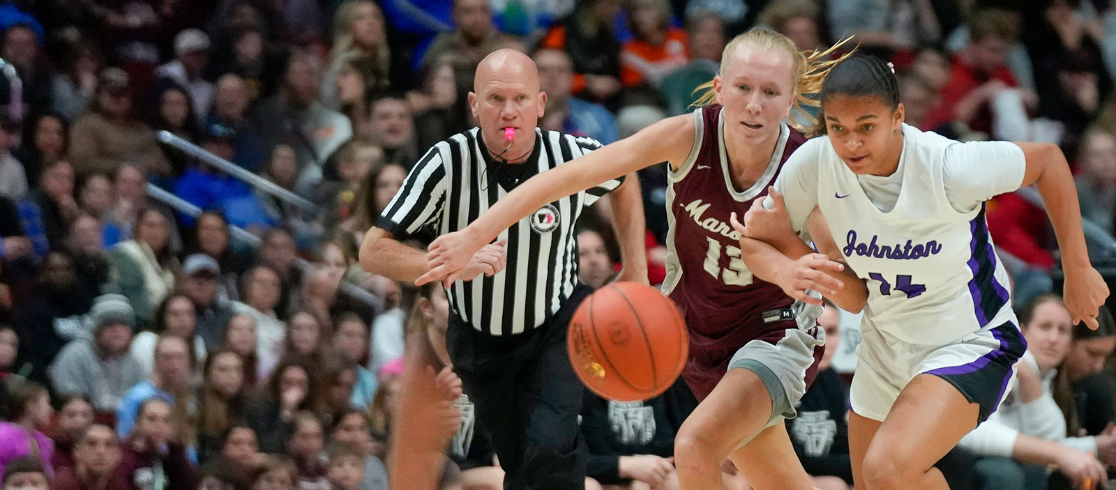 Two basketball players running after the ball with a referee behind them