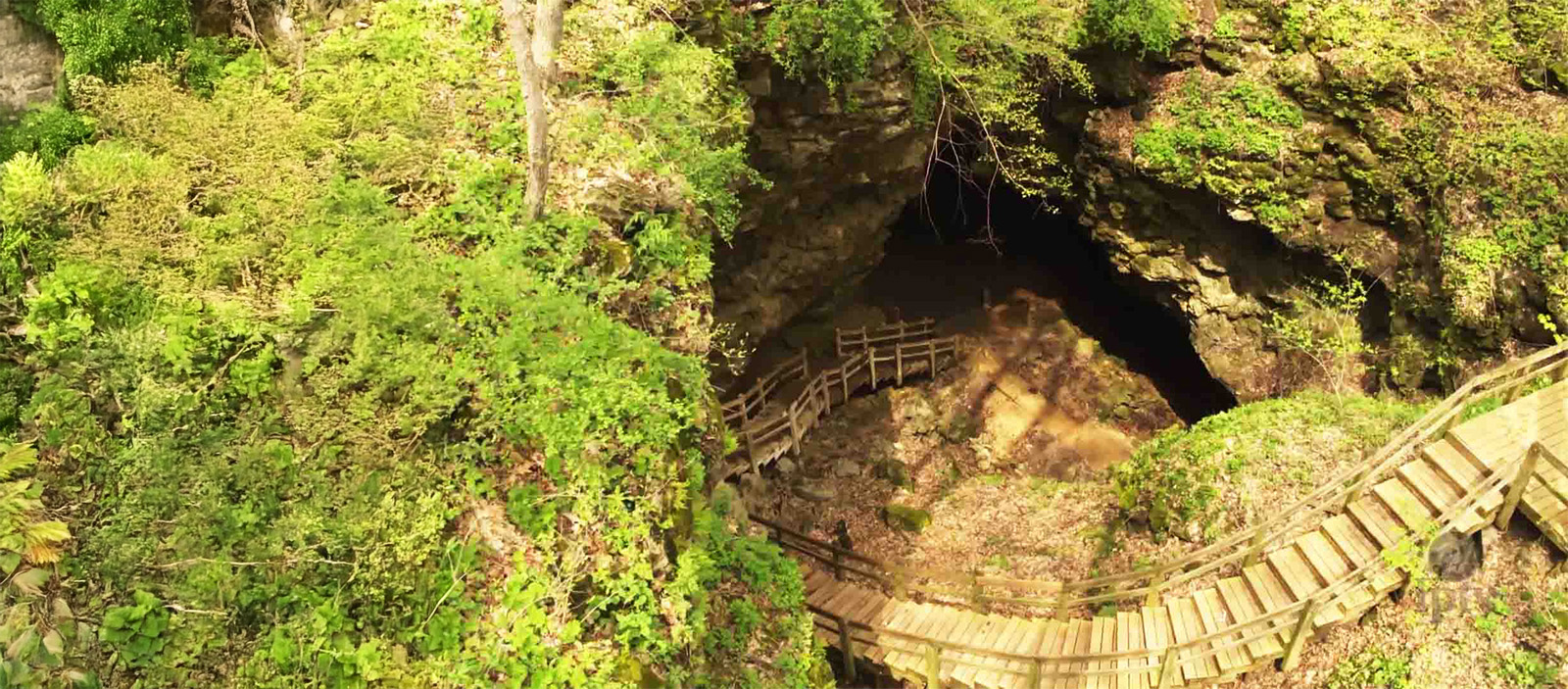 A wooden spiral staircase leading down into a cave.