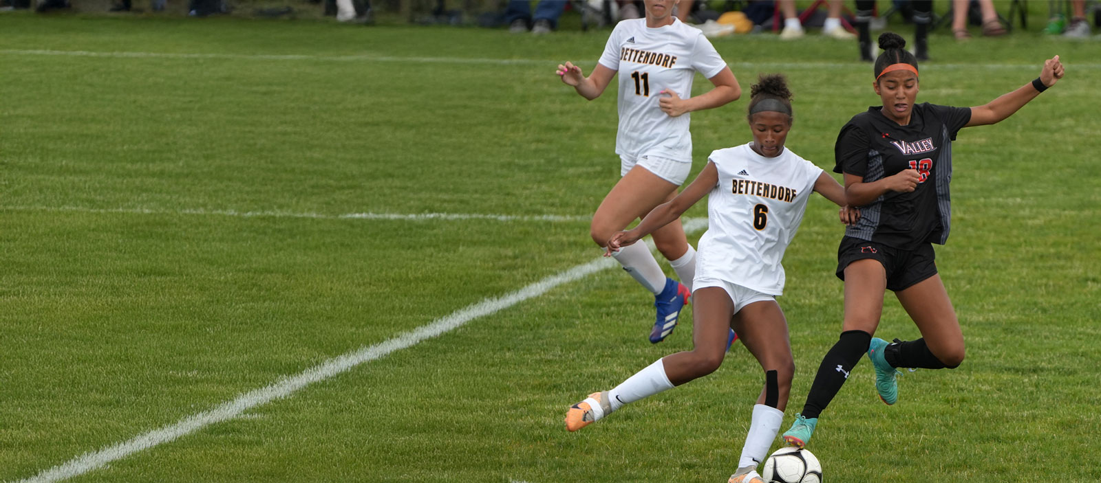 Two high school soccer players fight for the ball while a third player comes up behind them