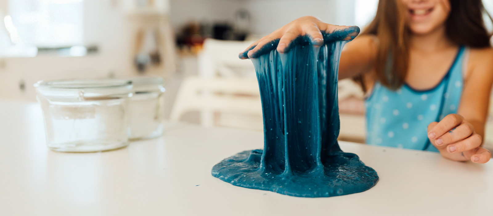 A young girl lifts her hand out of homemade slime making it cascade back down to the counter like a waterfall.