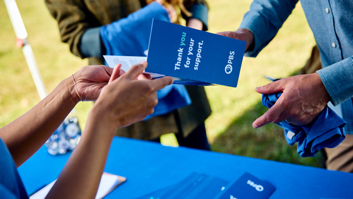 A person is handed a brochure that says, Thank you for your support.