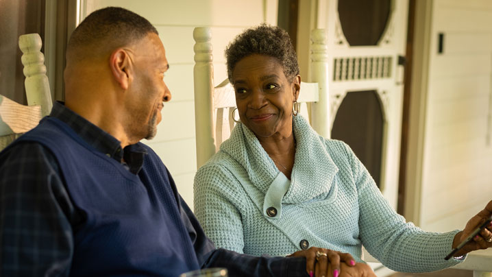 A man and woman sit on their front porch talking.