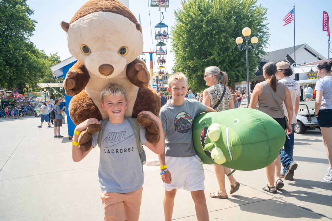 Two boys walking at the Fair with a giant stuffed bear