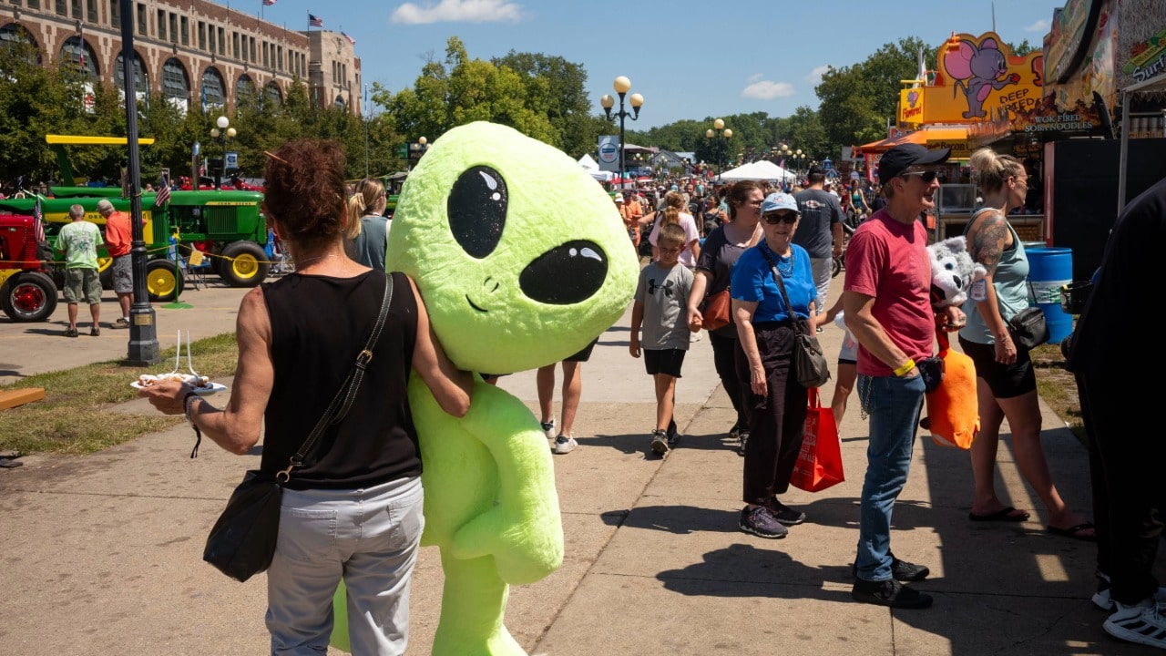Woman walking the fairgrounds with a giant stuffed alien prize