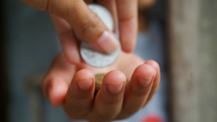 A hand holds coins as another person's hand adds more coins.