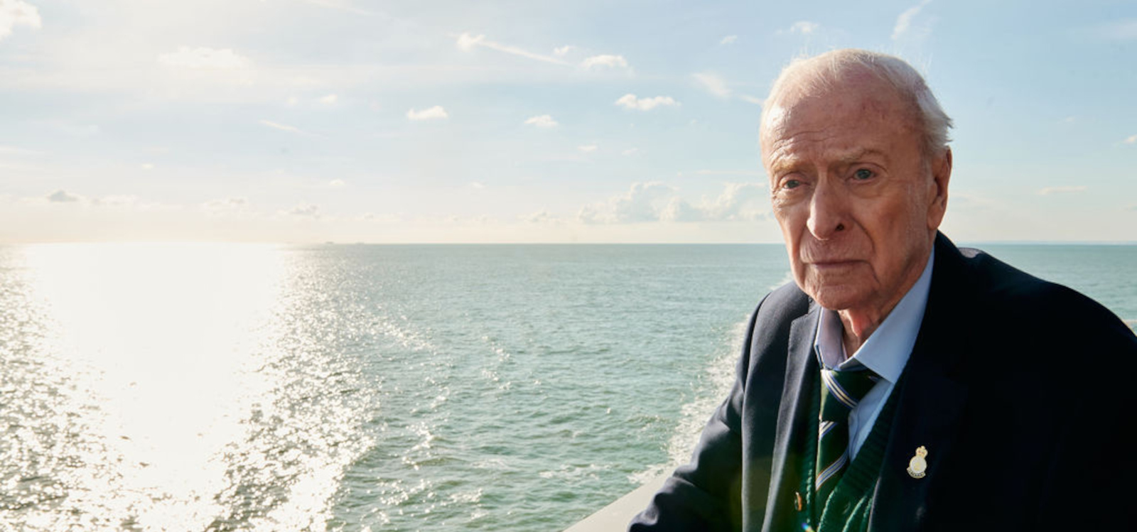 An old man in a suit standing near the ocean