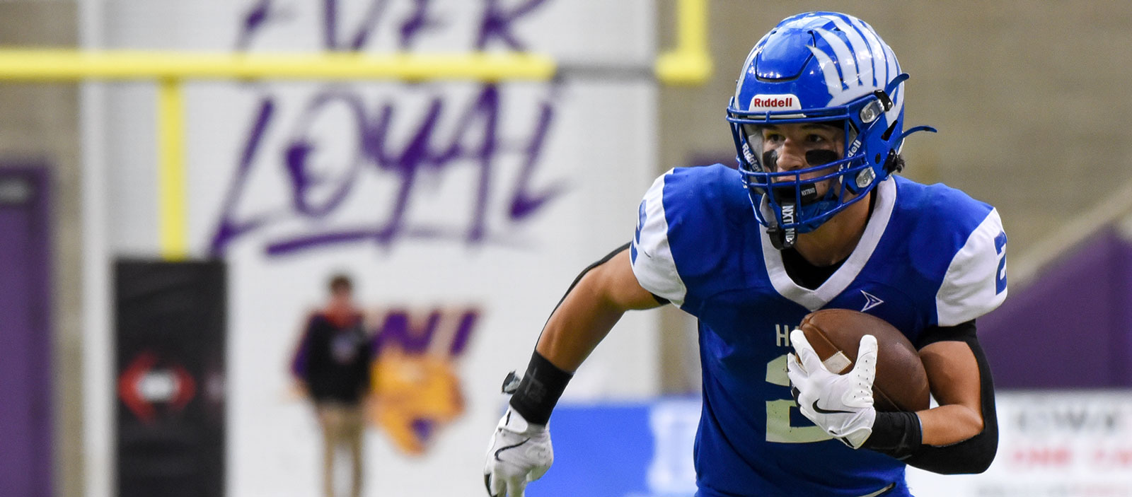 A high school football player holding a ball and running
