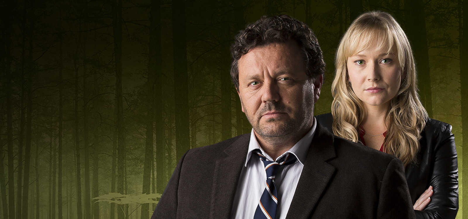 A man and a woman standing in front of a dimly lit forest background.