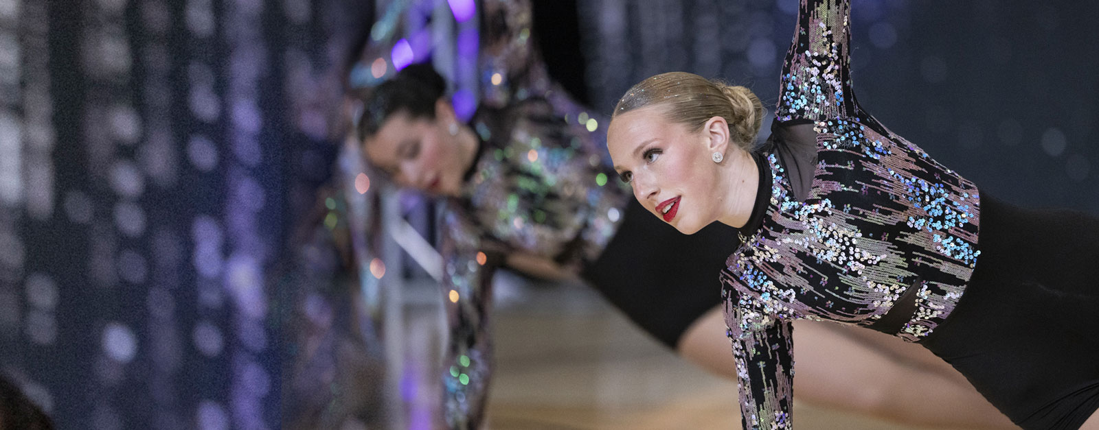 Two teenage girls wearing black and silver sparkle costumes dance on stage.