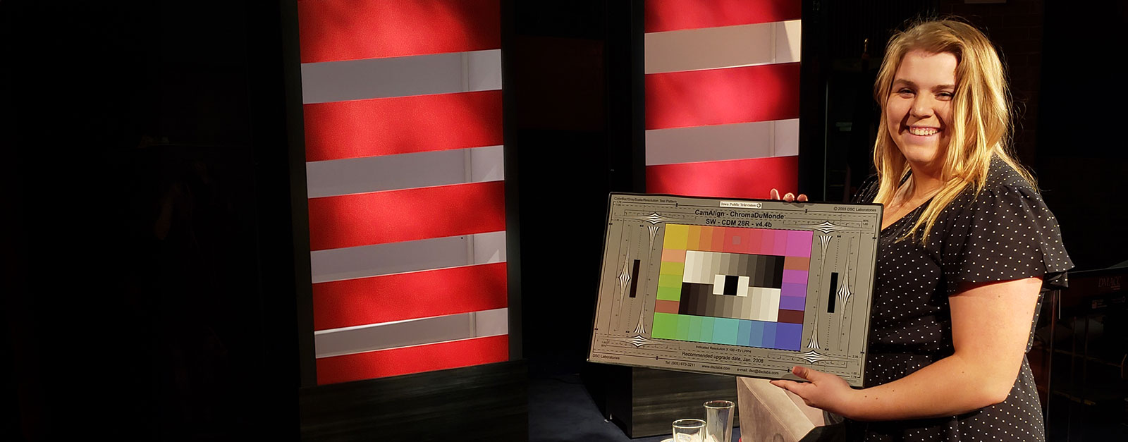 Person holding a color calibration chart in front of a red and white striped background.