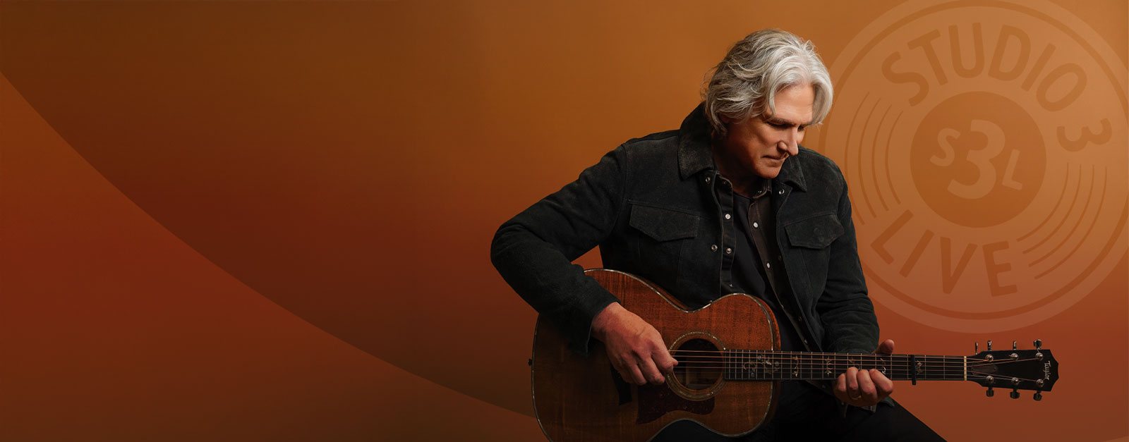 A man sits while playing a guitar.
