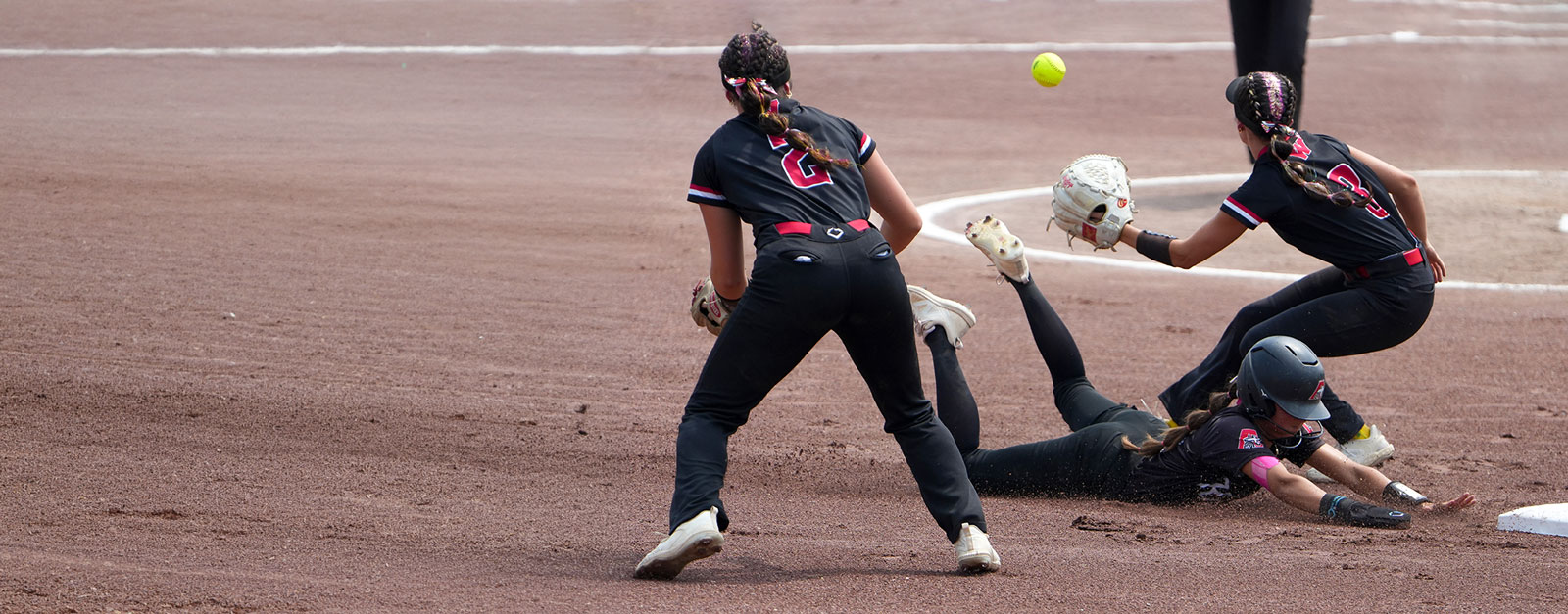 The player at first base prepares to catch a ball as the runner slides toward the base.