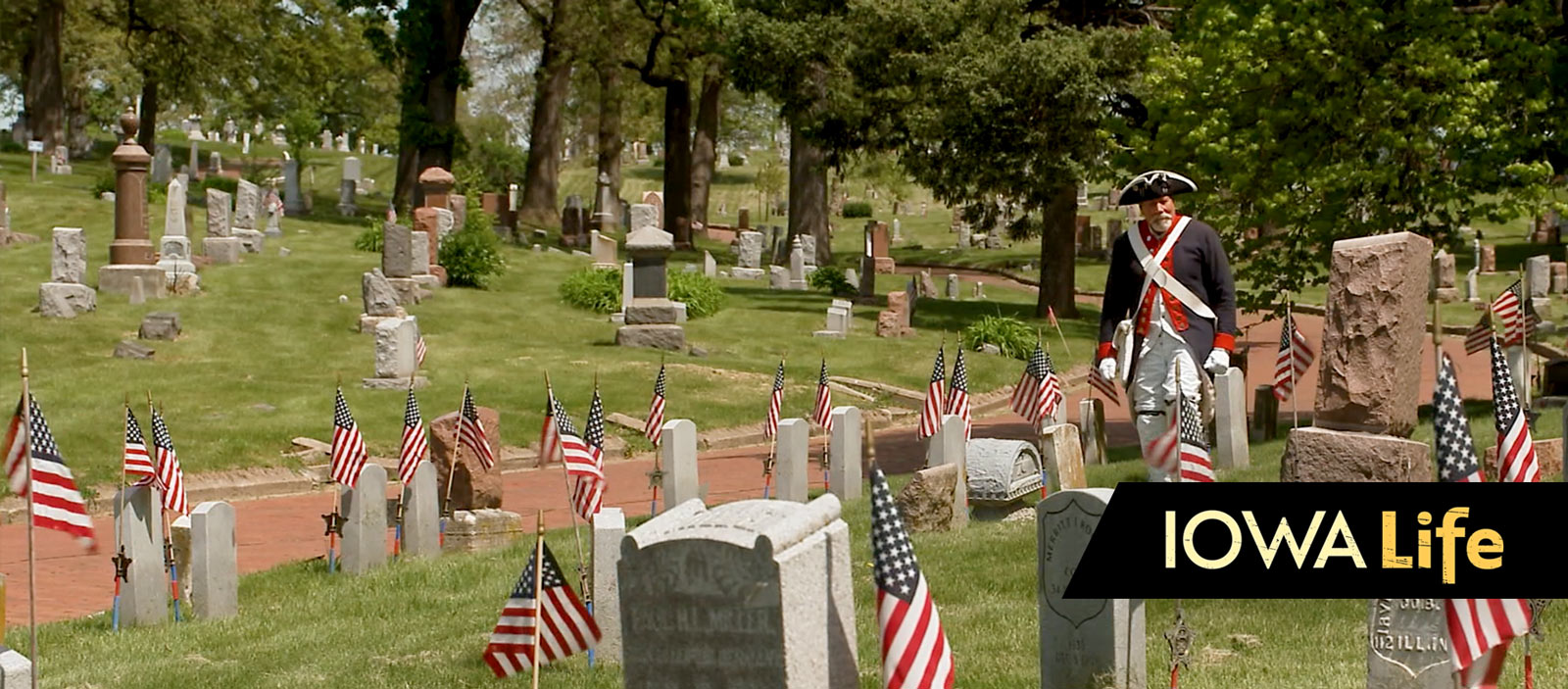 A man dressed in a military uniform walks through a graveyard.