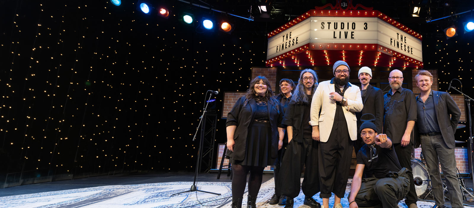 Eight members of The Finesse pose under the Studio 3 LIVE marquee.