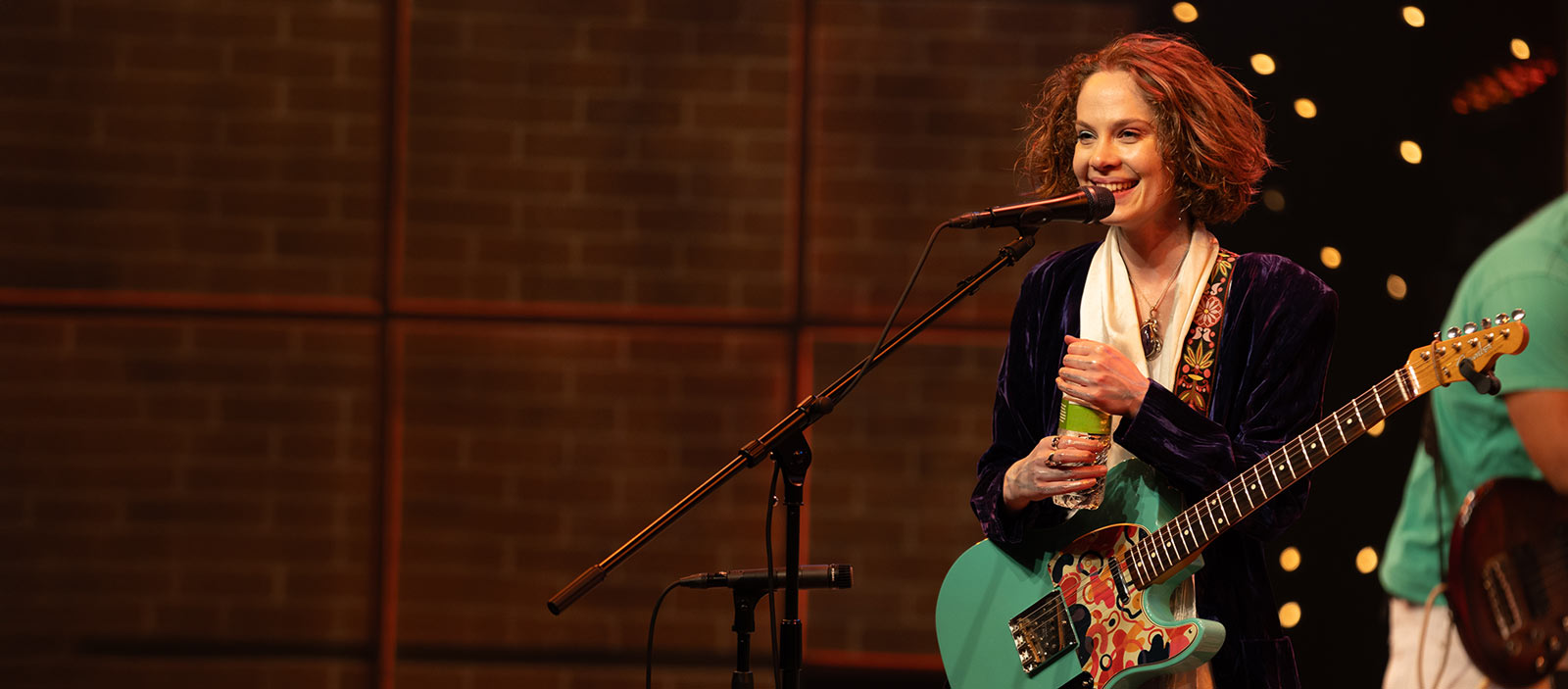 A young woman with red hair plays a green guitar.