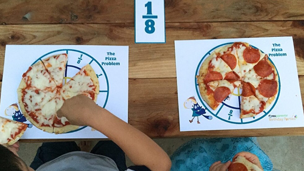 Two children sitting in front of their personal pizza on the pizza placemat with the one eighth fraction card above their personal pizza.