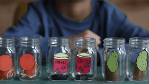 Six jars in a row in front of a young child. From left to right there are two jars with a drawing of an orange on them, two jars with text on them and two jars with a drawing of a potato on them.