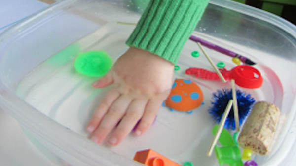 A child’s hand putting toys in a bowl of water.