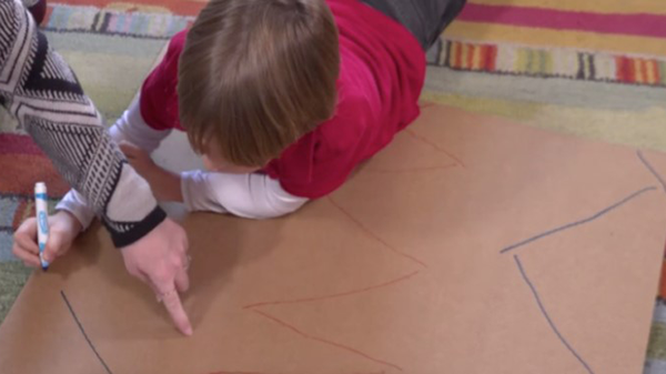 A young boy drawing lines on a piece of cardboard.