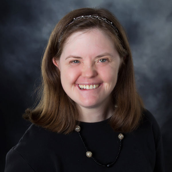 A young woman with shoulder length brown hair and blue eyes smiles in a professional photo. 