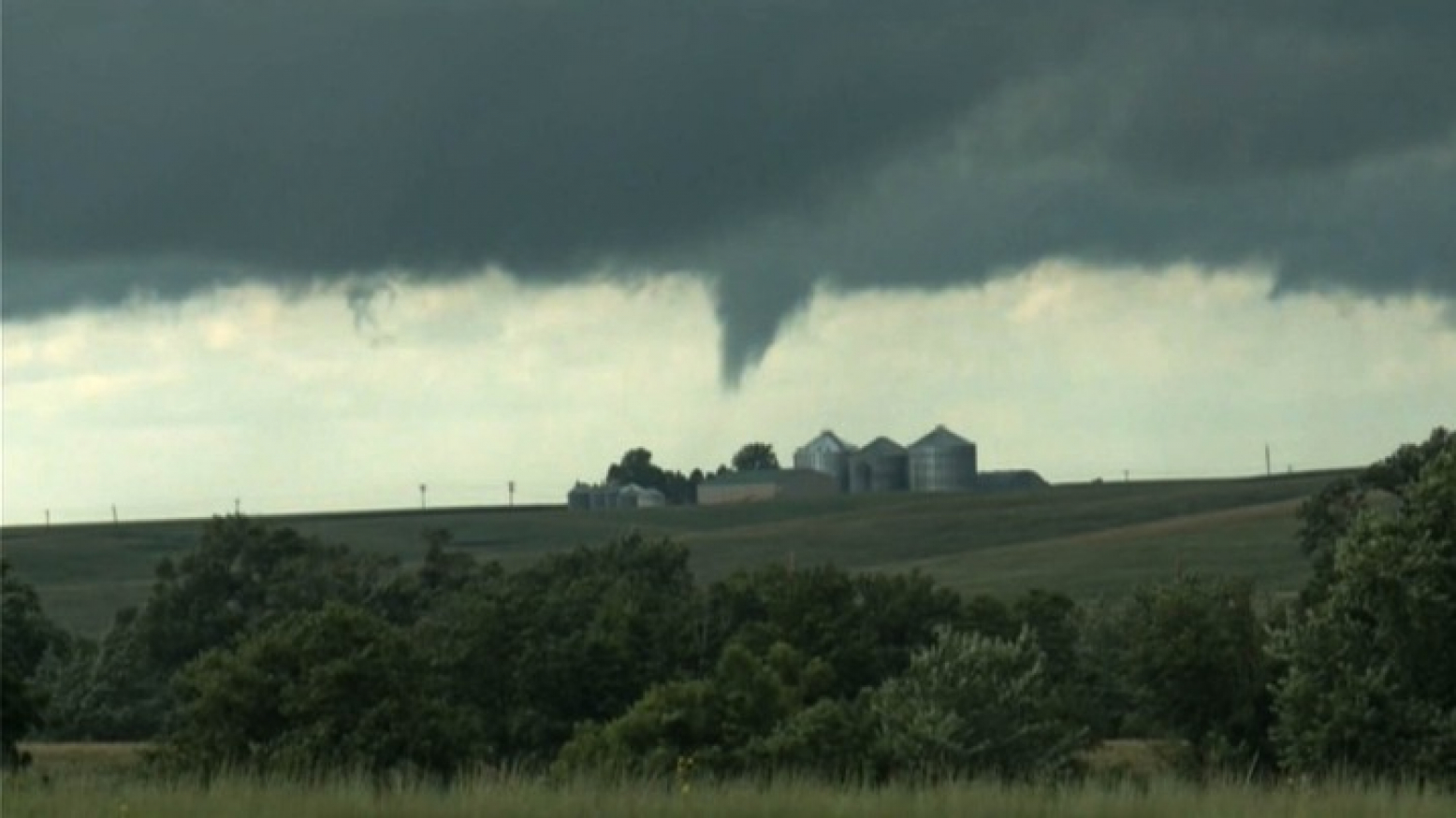 A funnel cloud appears to be forming over a farm