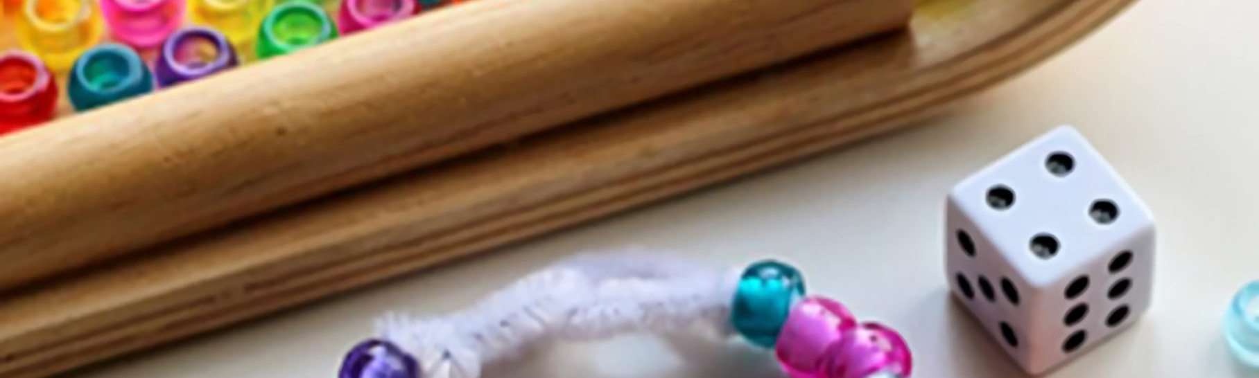 A basket full of beads with a playing dice and a bracelet in front.