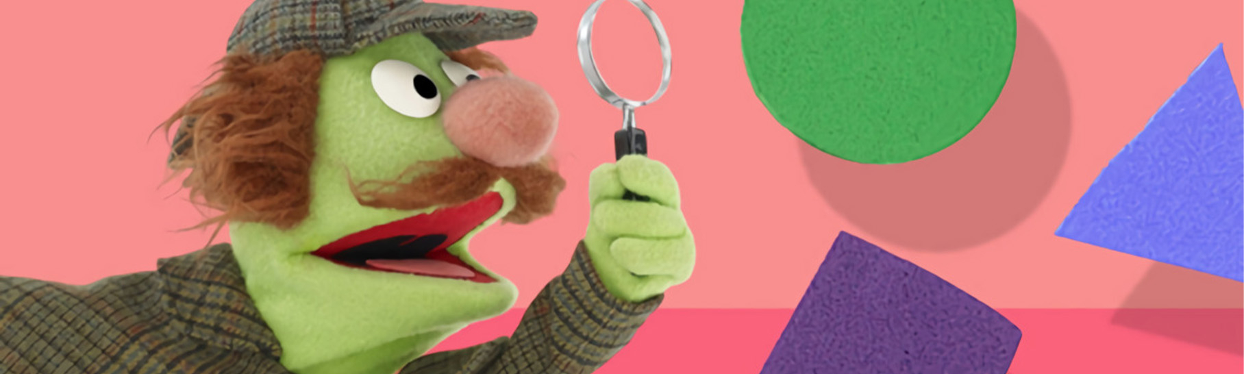 A sesame street character dressed like a detective using a magnifying glass and looking at a triangle, square and circle.
