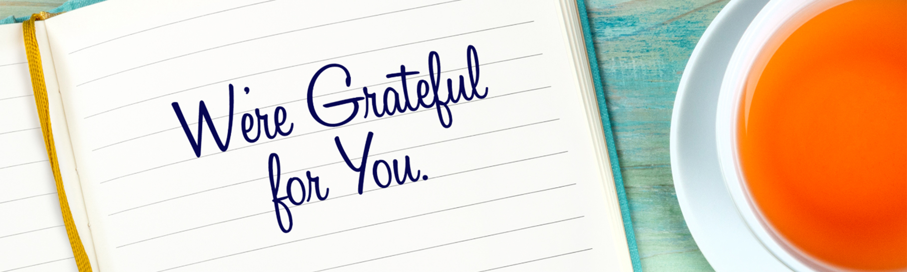 "We're Grateful for You" written in a notebook next to a cup of coffee.