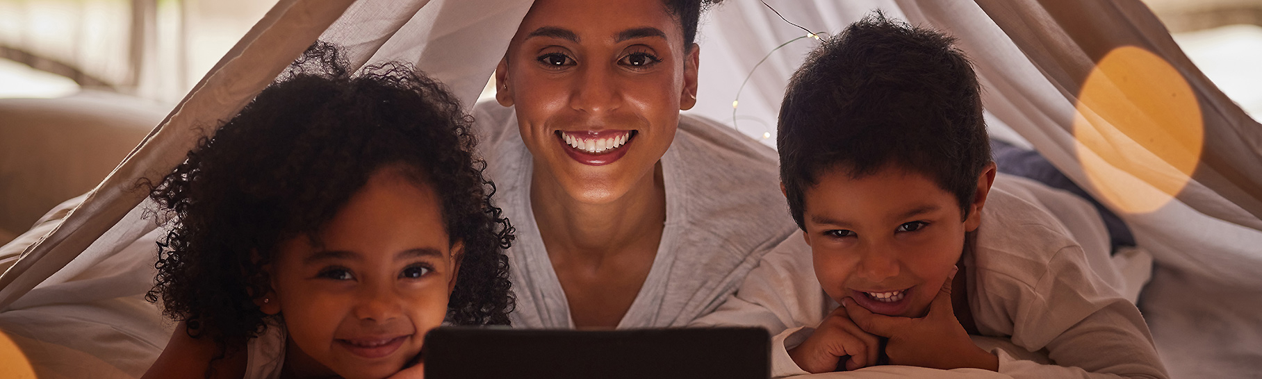 A mother watches PBS KIDS Read-Alongs on a tablet with her young daughter and son.