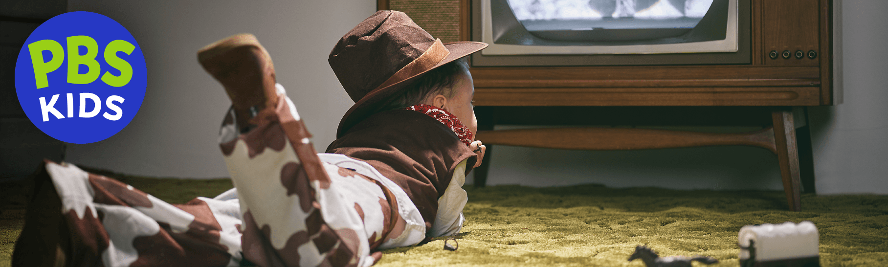 A nostalgic photo of a boy in a cowboy costume laying on the floor watching his favorite cowboy TV program.