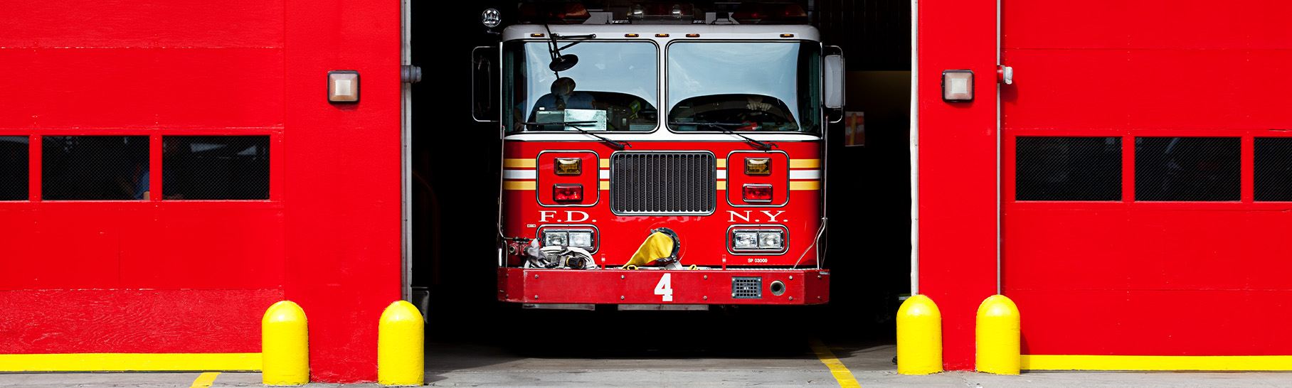 A red fire truck parked inside a fire station garage with a partially open door.