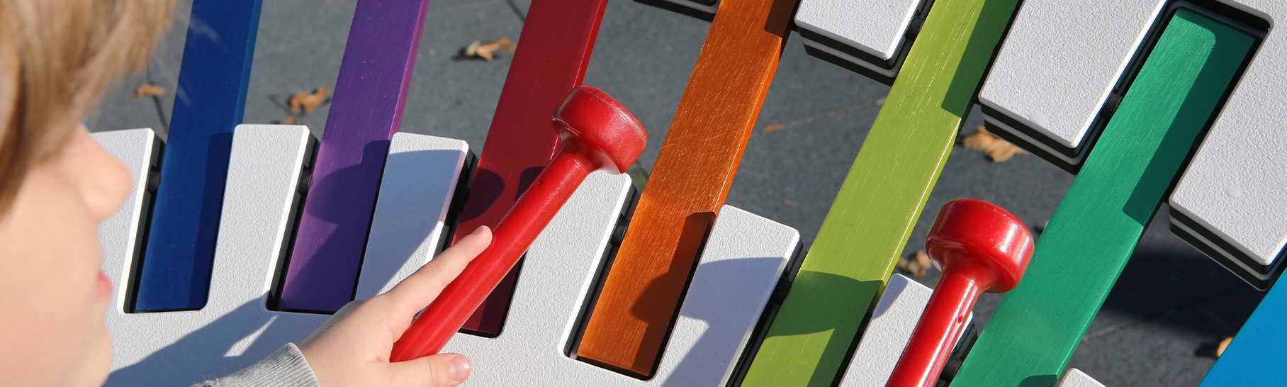 A child playing on a large rainbow colored outdoor xylophone.