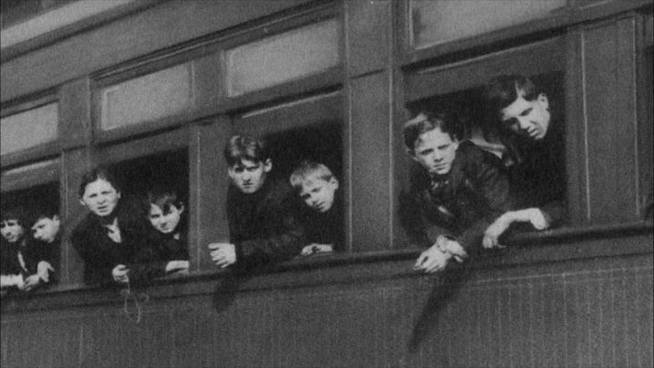 a black and white image of young boys hanging out the windows of a train.