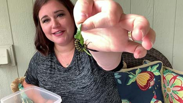 woman holding a caterpillar on a leaf to the camera 