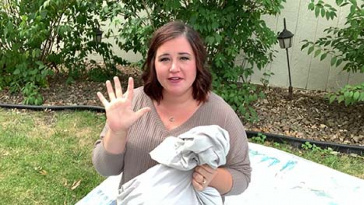 Woman holding her hand up toward the camera with a pillow case in her other hand.