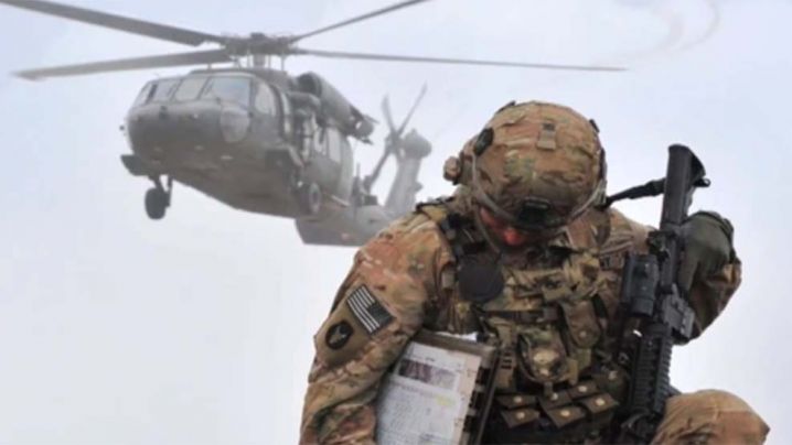 solider kneeling with a Blackhawk helicopter in the background 