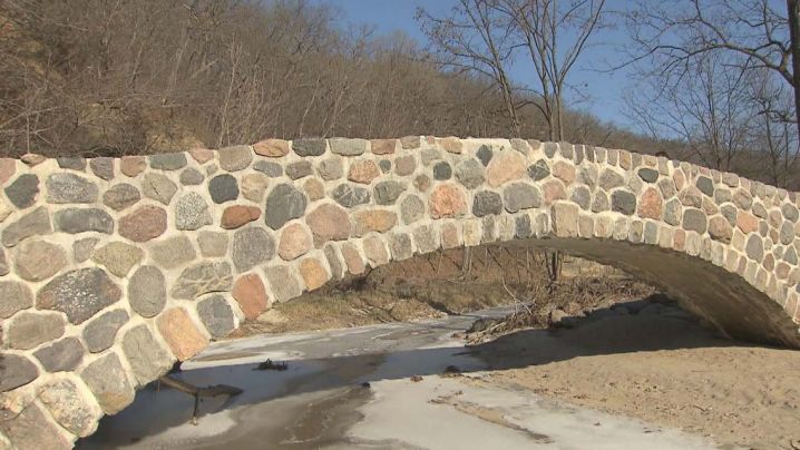 A man-made stone bridge arches over a stream.
