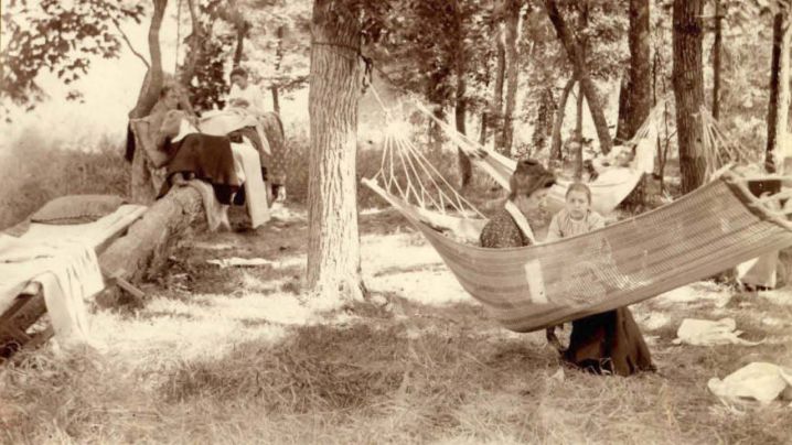 A mother and child sit in a hammock under shady trees.