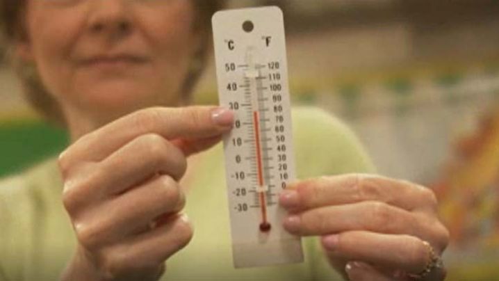 a woman holding up a thermometer, showing the temperature scales Celsius and Fahrenheit
