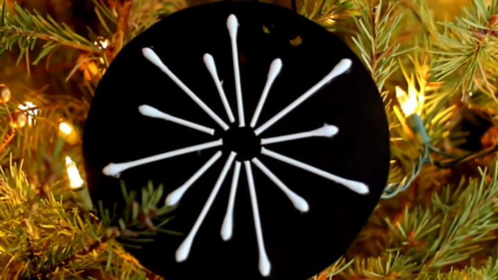A cotton swab snowflake hanging on a tree.