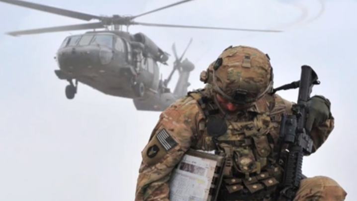 solider kneeling as a Blackhawk helicopter flies over head.