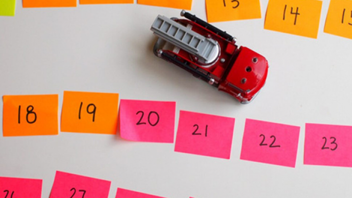 A toy firetruck surrounded in a road pattern by multicolored sticky notes with numbers on them.