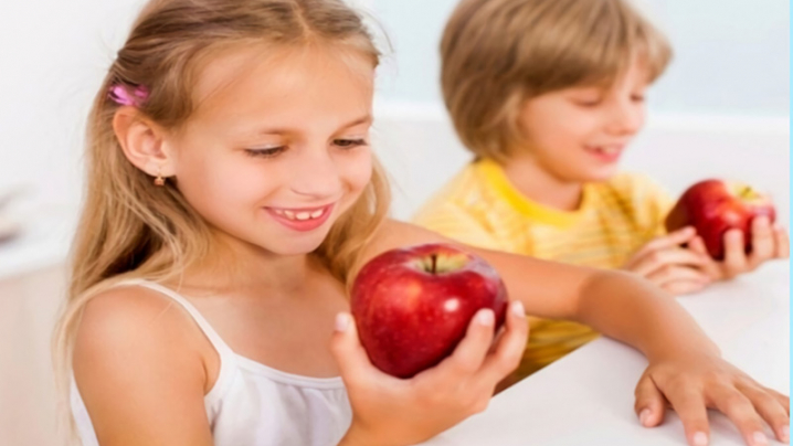 A young girl and boy holding apples.