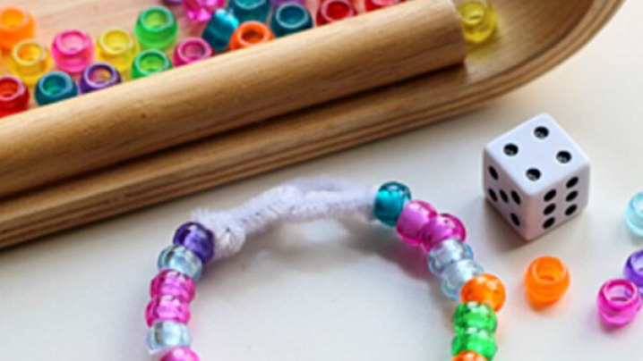 A basket full of beads with a playing dice and a bracelet in front.