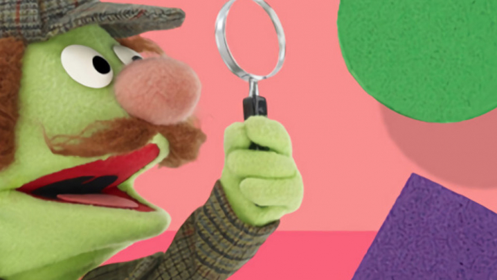 A sesame street character dressed like a detective using a magnifying glass and looking at a triangle, square and circle.