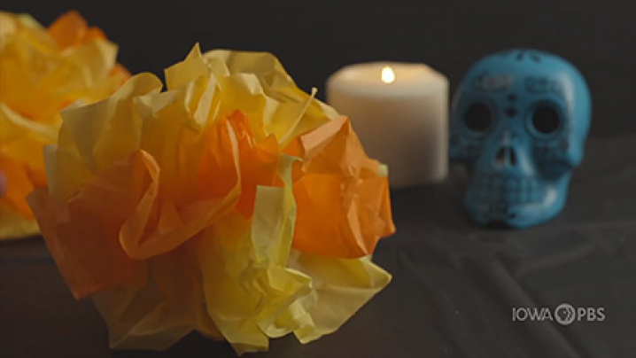 Tissue paper marigolds, a skull, and a lit candle sit on a table.